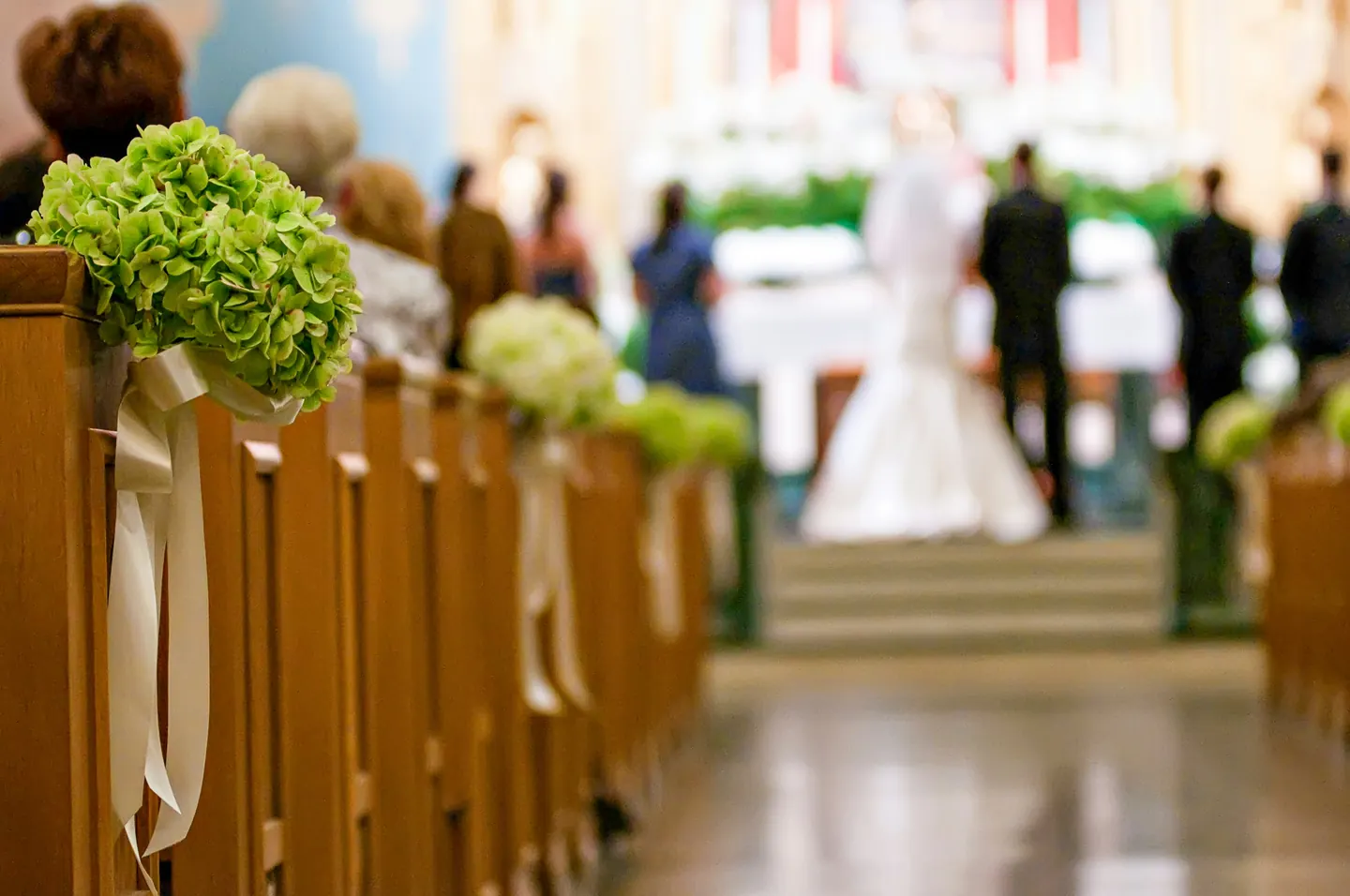 Blumenschmuck an den Kirchenbänken, im Hintergrund ein Brautpaar am Altar